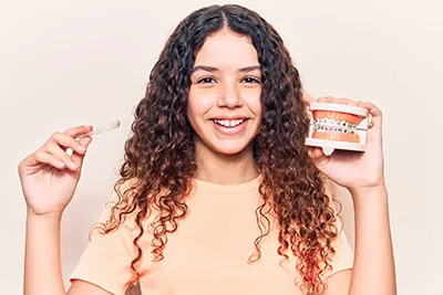 young patient holding up a dental model of braces and clear orthodontic aligners