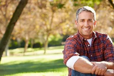 man with dentures smiling while sitting in a park